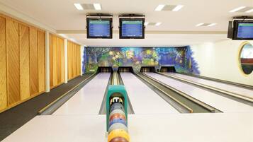 A bowling alley with multiple lanes, wooden paneling on the walls, and two monitors displaying scores.