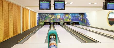 A bowling alley with multiple lanes, wooden paneling on the walls, and two monitors displaying scores.