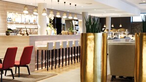 A modern hotel lobby with a bar area, seating, and decorative plants.