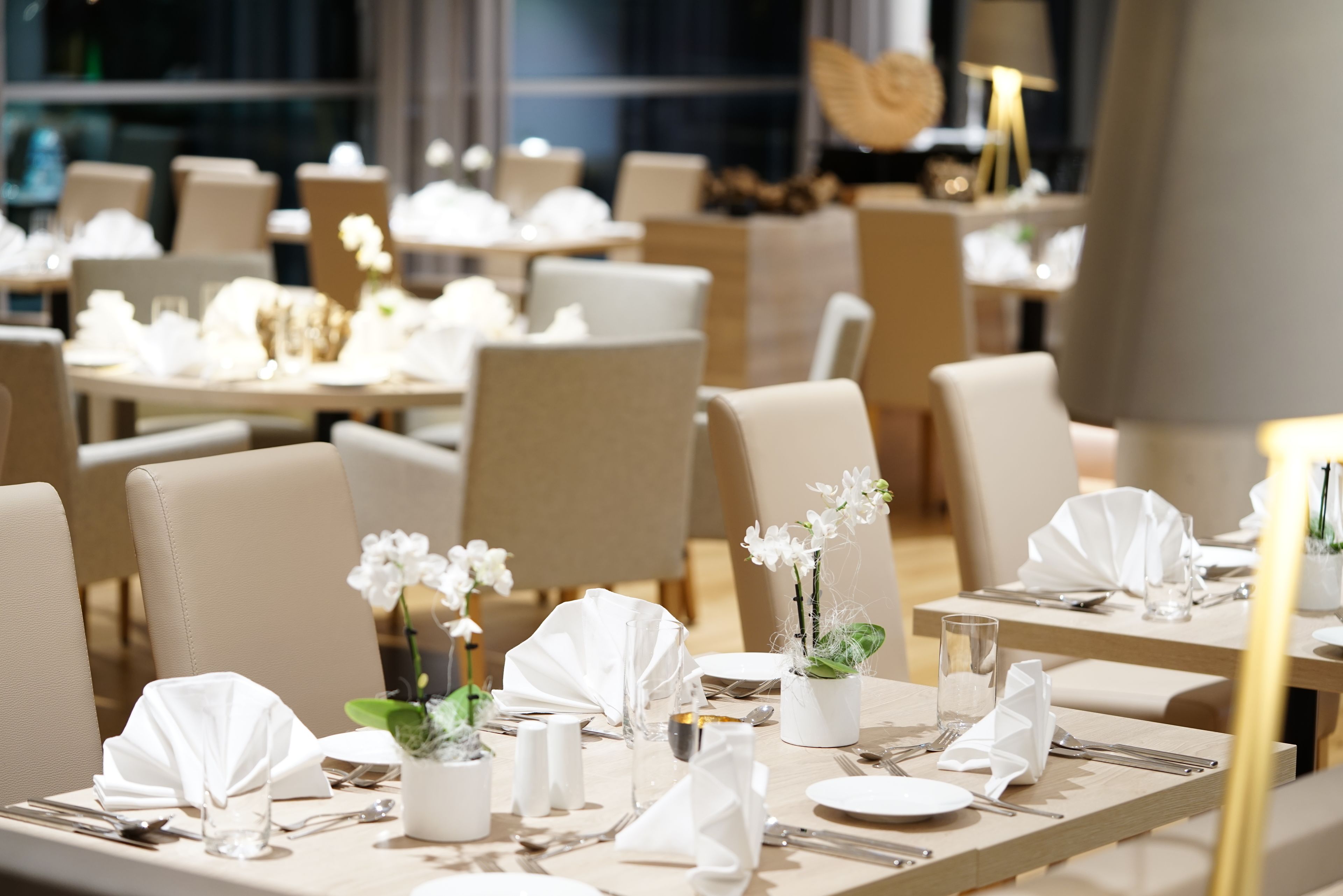 Un restaurant où les tables sont disposées avec soin, recouvertes de nappes blanches et agrémentées d’orchidées blanches.