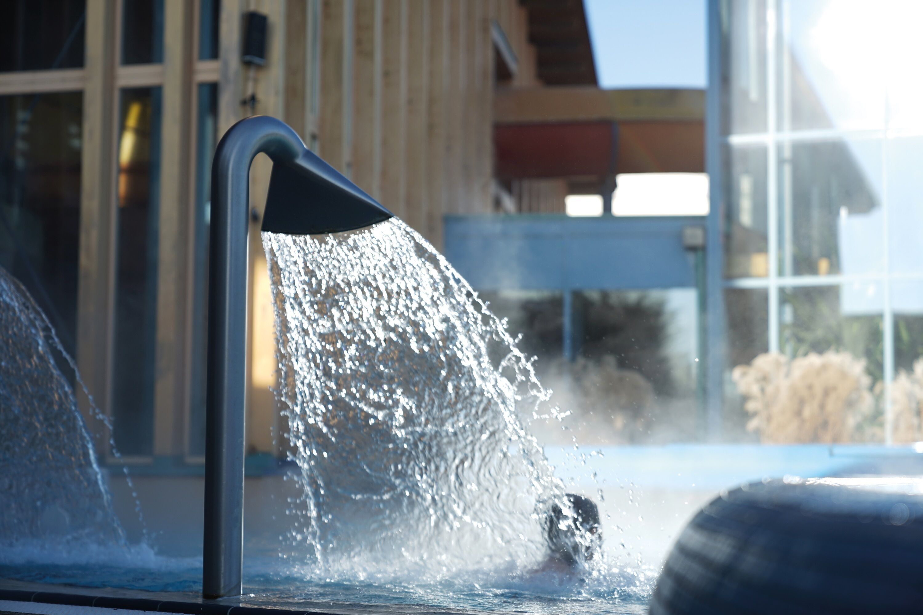 A water feature with a spout, a building with large windows, and a clear sky.