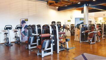 Uma academia com diversos equipamentos de exercício, piso de madeira e um relógio na parede.