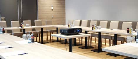 Un salón de conferencias con largas mesas, sillas, un proyector y botellas de agua.