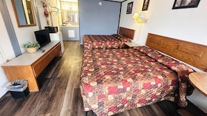 Un dormitorio con cama, escritorio, televisor y una pequeña cocina americana.