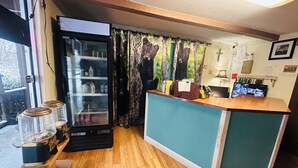 Zona de recepción con mostrador de madera, refrigerador y ventana con cortinas.