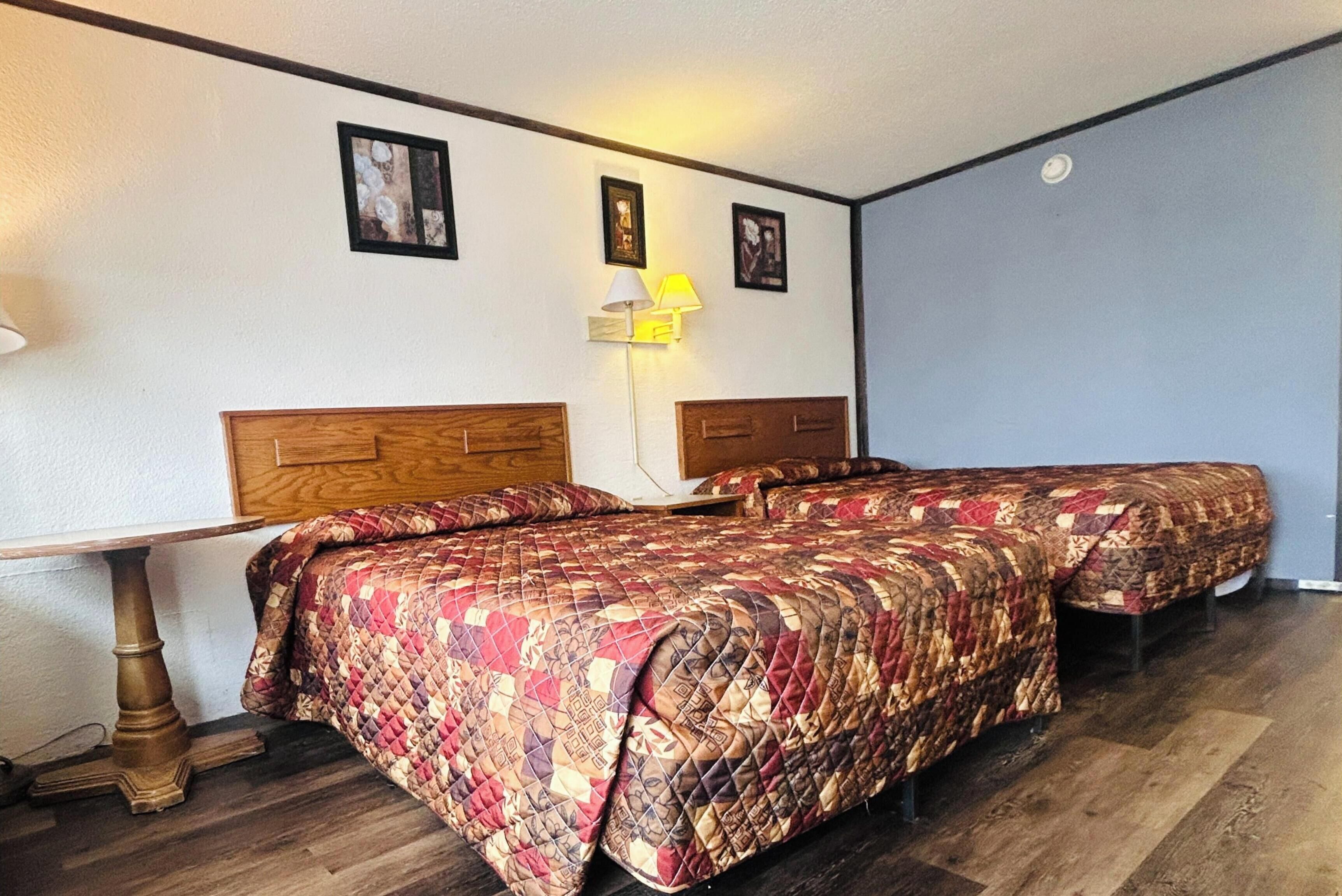 A room with two beds, a table, and a lamp.