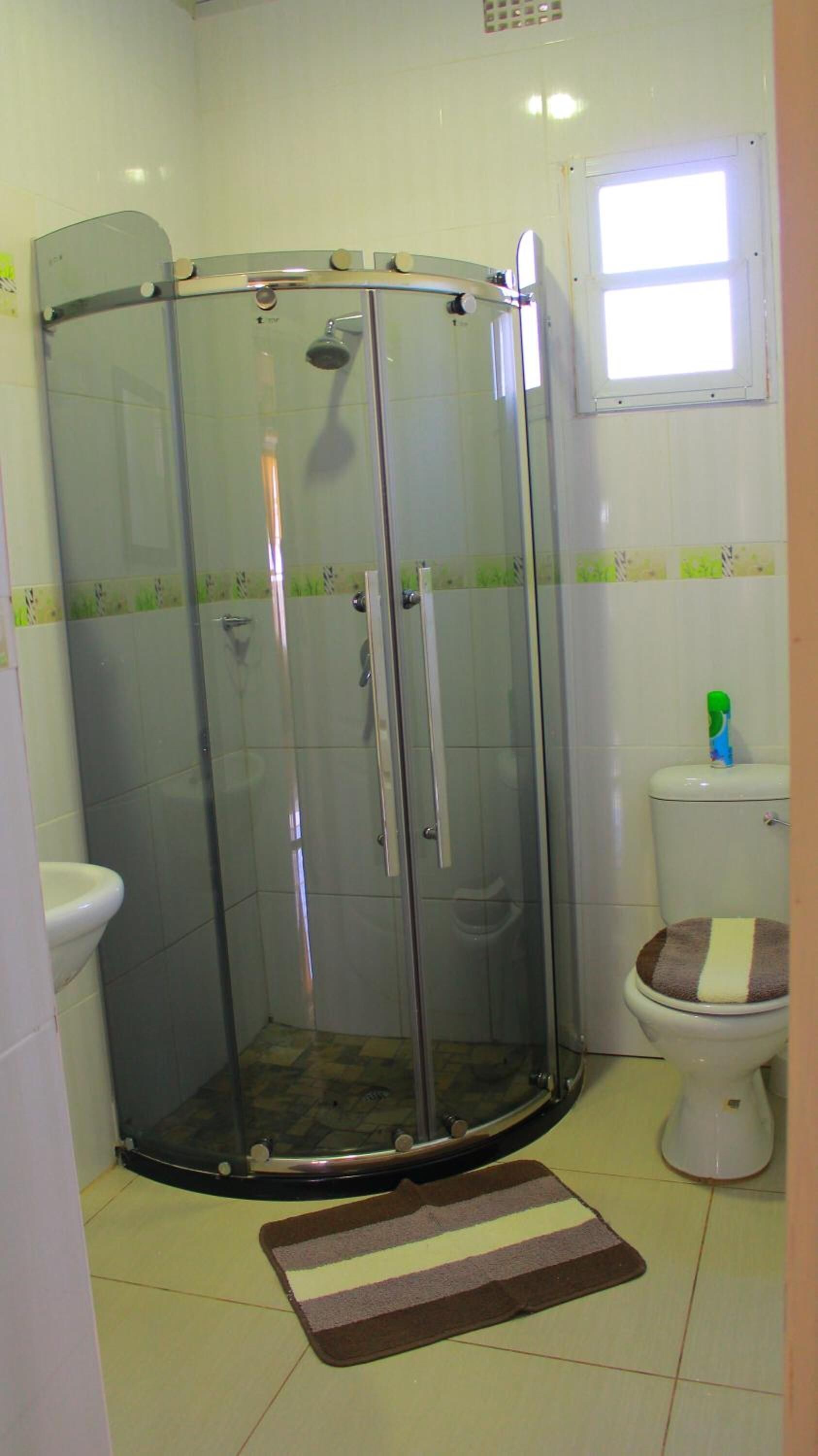 A bathroom with a glass shower enclosure, a toilet, and a small window.