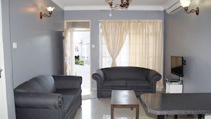 Una sala de estar con dos sofás, una mesa de centro, un televisor de pantalla plana y una ventana con cortinas.