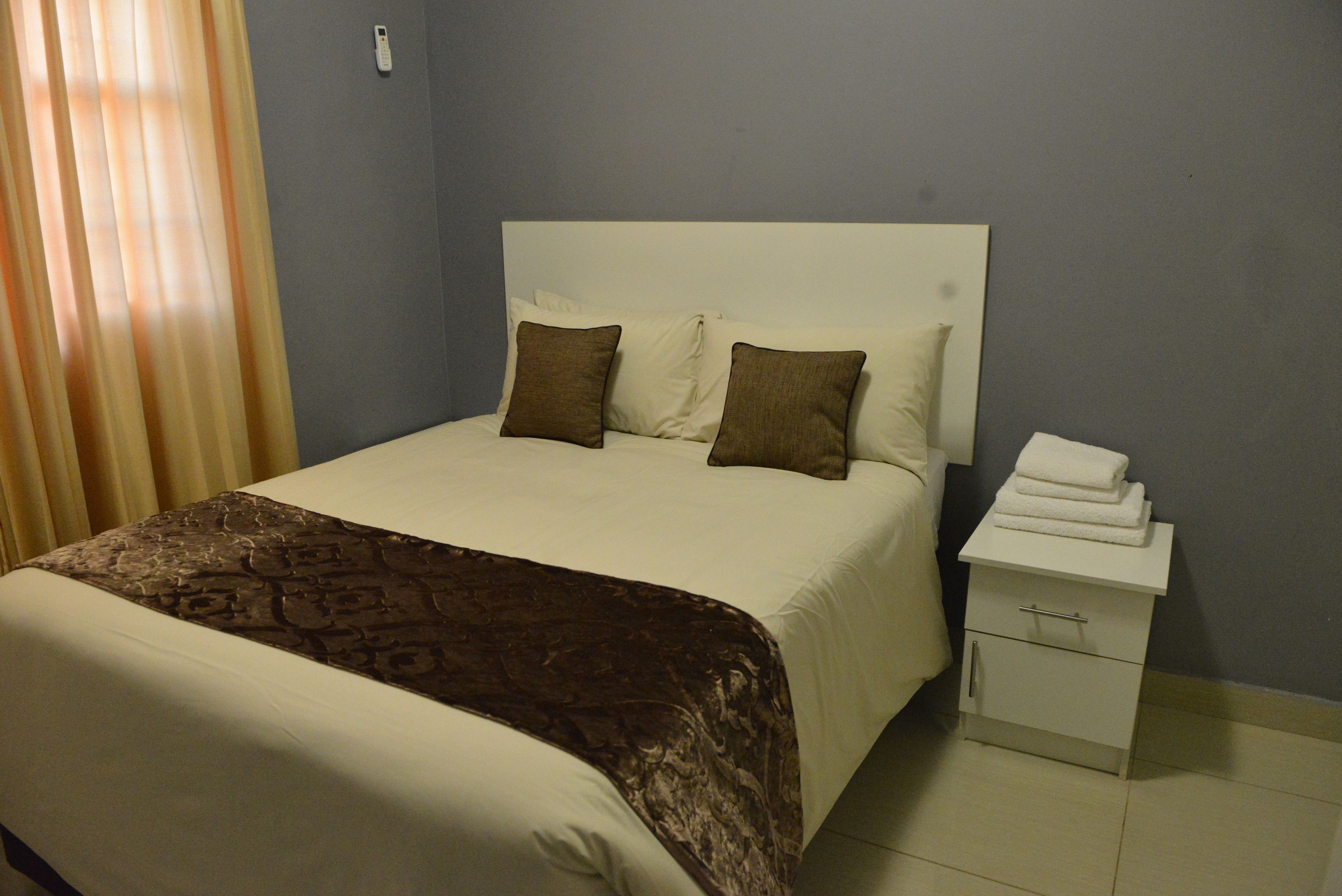 A neatly made bed with a patterned bedspread, two pillows, and a white nightstand with a folded towel.
