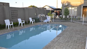 Una piscina con una terraza empedrada, rodeada de sillas blancas y una valla blanca.