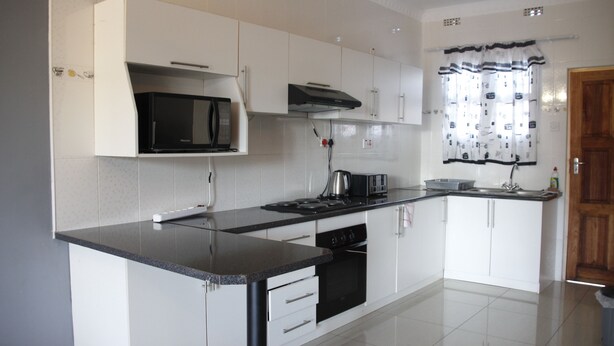 Una cocina moderna con armarios blancos, encimera negra, microondas, estufa y fregadero.