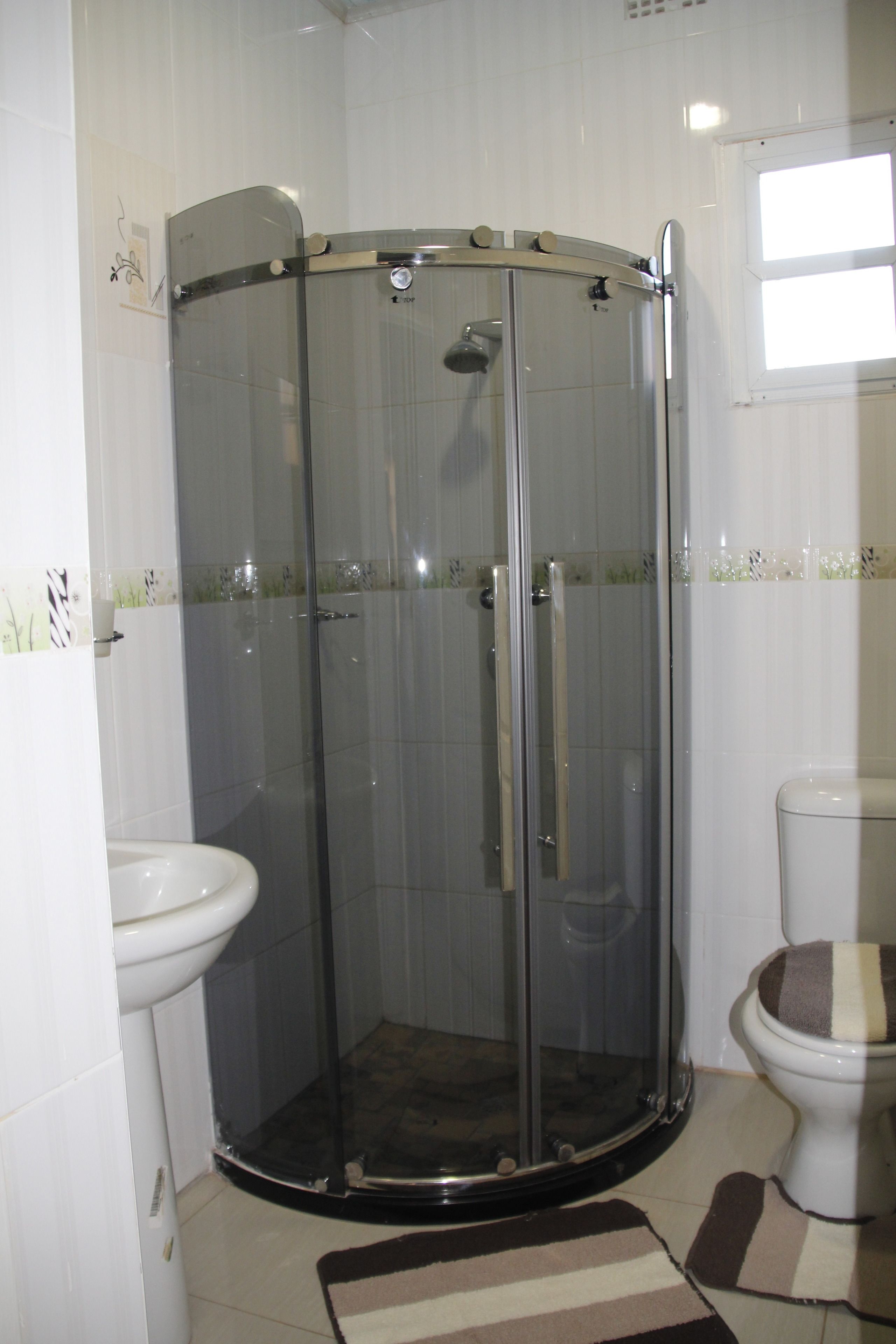 Cabina de ducha con paredes de cristal, un inodoro y un lavamanos blancos en un baño.