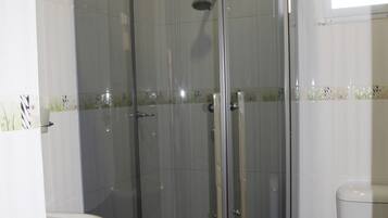 Cabina de ducha con paredes de cristal, un inodoro y un lavamanos blancos en un baño.