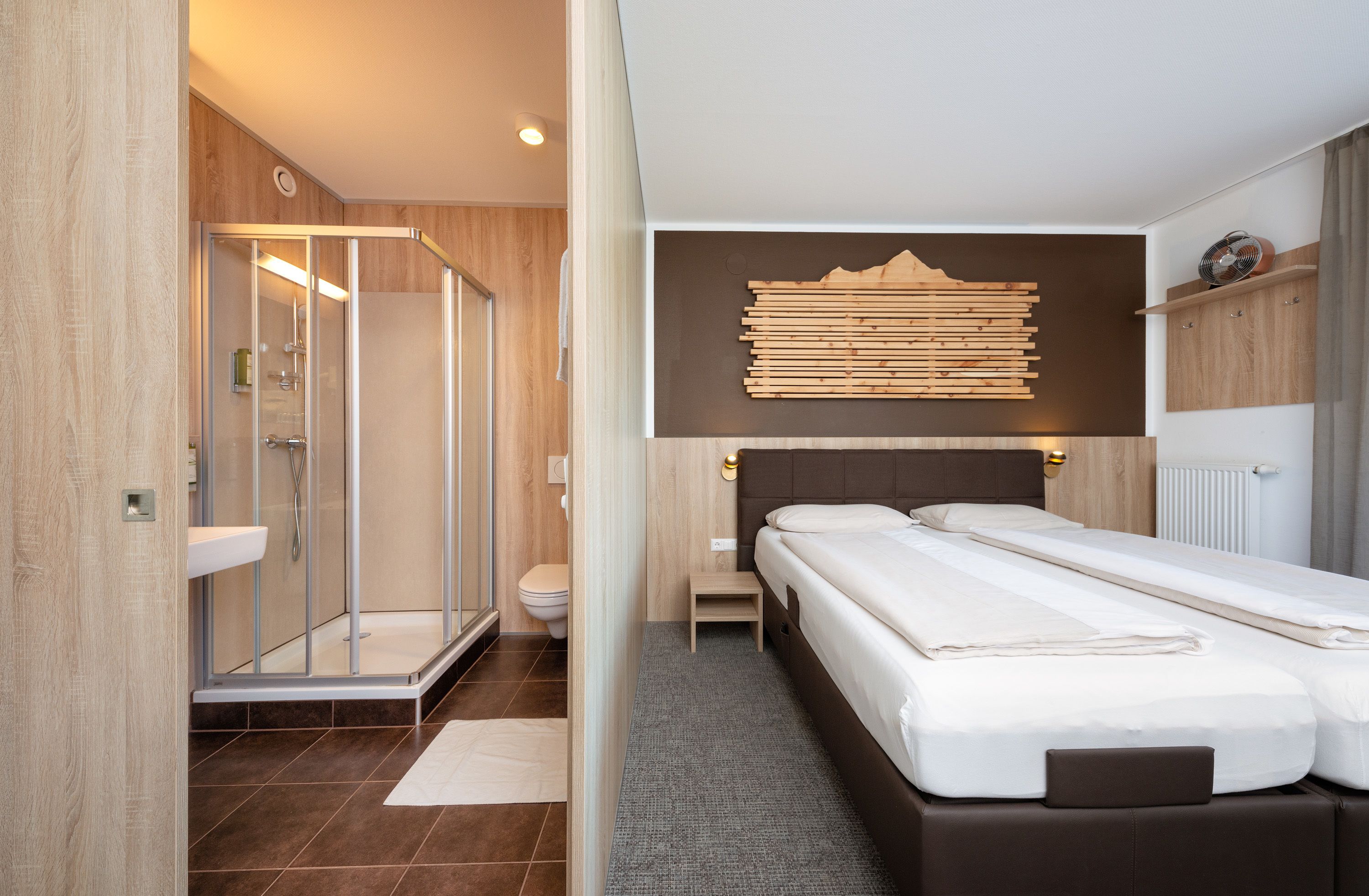 A modern hotel room with a shower, toilet, and a bed with two pillows.