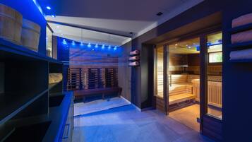 Un área de spa moderna con sauna de vidrio, bancos de madera y techo iluminado en azul.