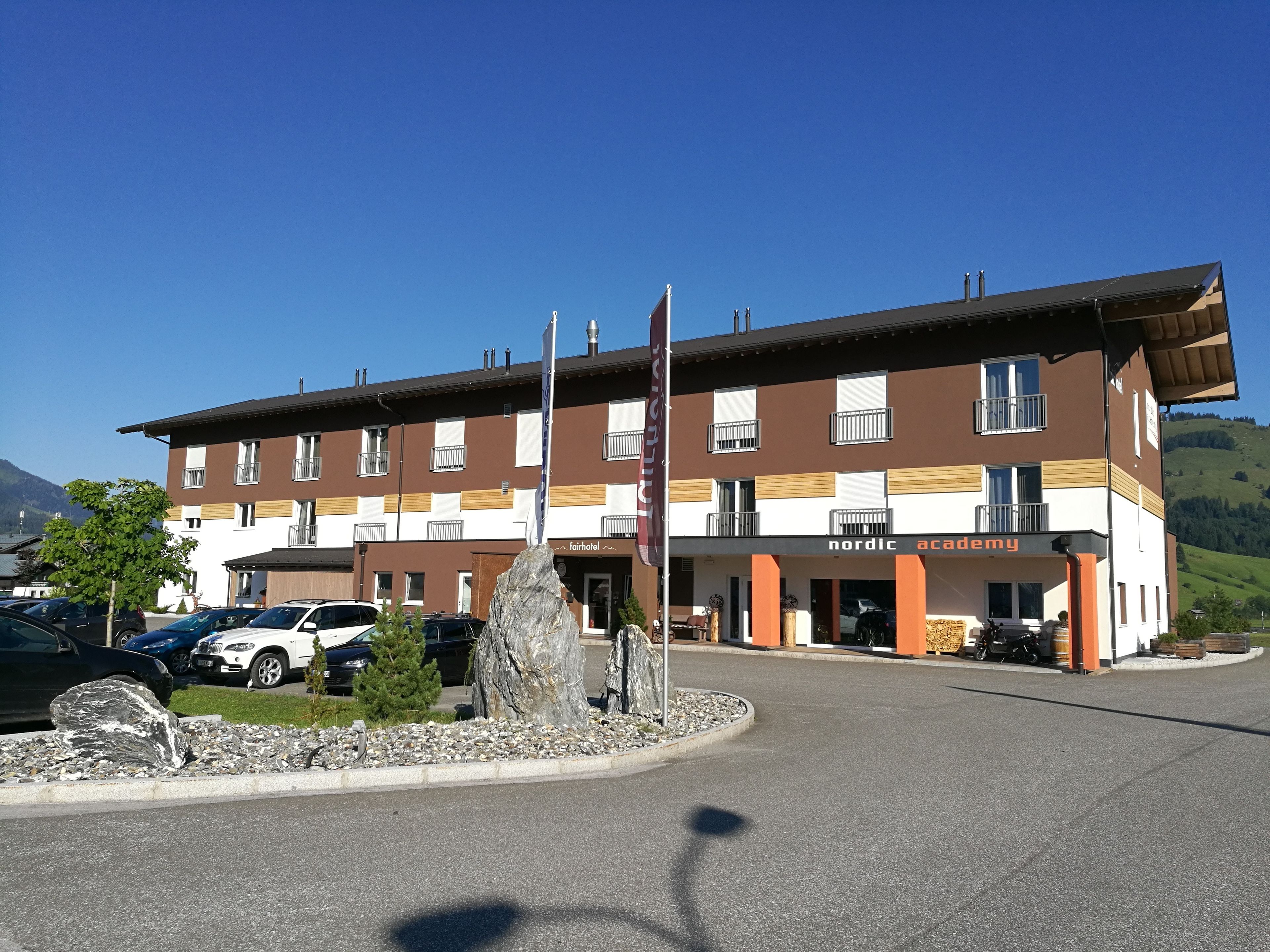 Un hotel de diseño moderno, con una entrada destacada, un asta de bandera y un área de estacionamiento con varios automóviles.