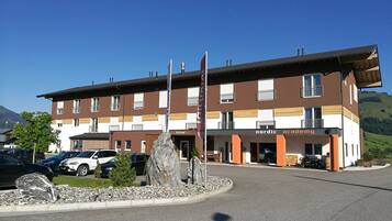 Un hotel de diseño moderno, con una entrada destacada, un asta de bandera y un área de estacionamiento con varios automóviles.
