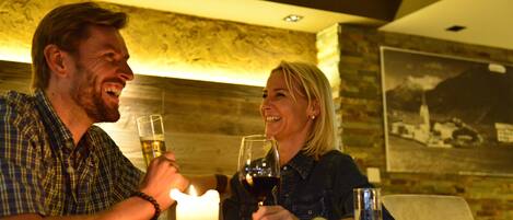 A man and a woman toasting with wine glasses at a table with a lit candle, in a room with a wooden wall and a framed picture.