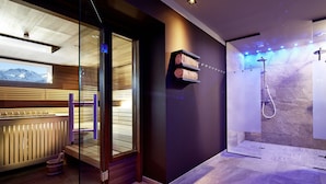 Un baño moderno con cabina de ducha de vidrio, bañera de madera y vistas a las montañas a través de un amplio ventanal.
