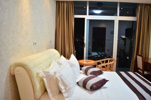 Una habitación de hotel con una cama grande, vistas de la ciudad por la noche y un balcón con mesa y sillas.