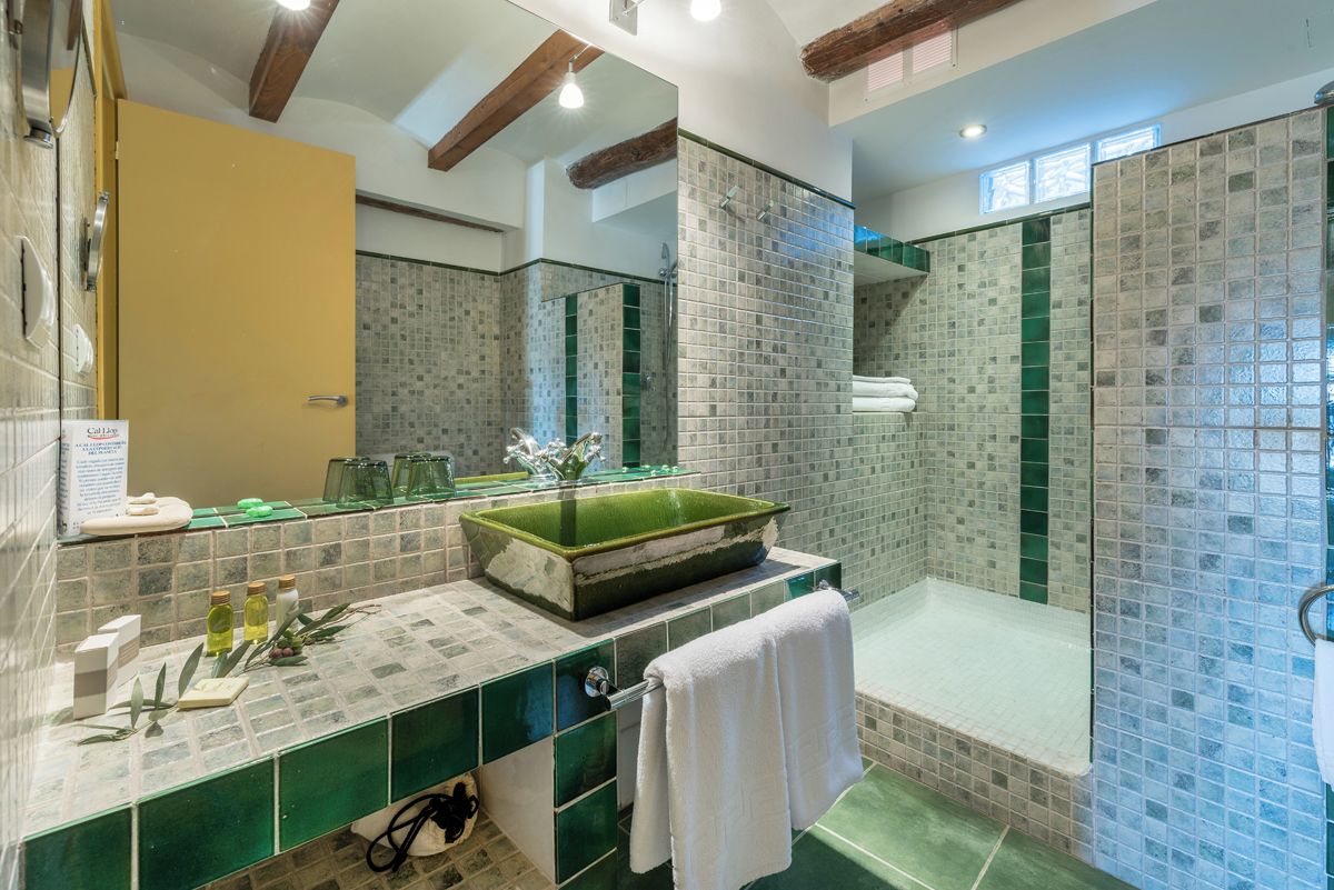 Un baño con lavamanos de azulejos verdes, lavabo de vidrio y zona de ducha con mosaicos.