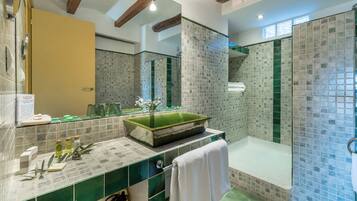 Un baño con lavamanos de azulejos verdes, lavabo de vidrio y zona de ducha con mosaicos.