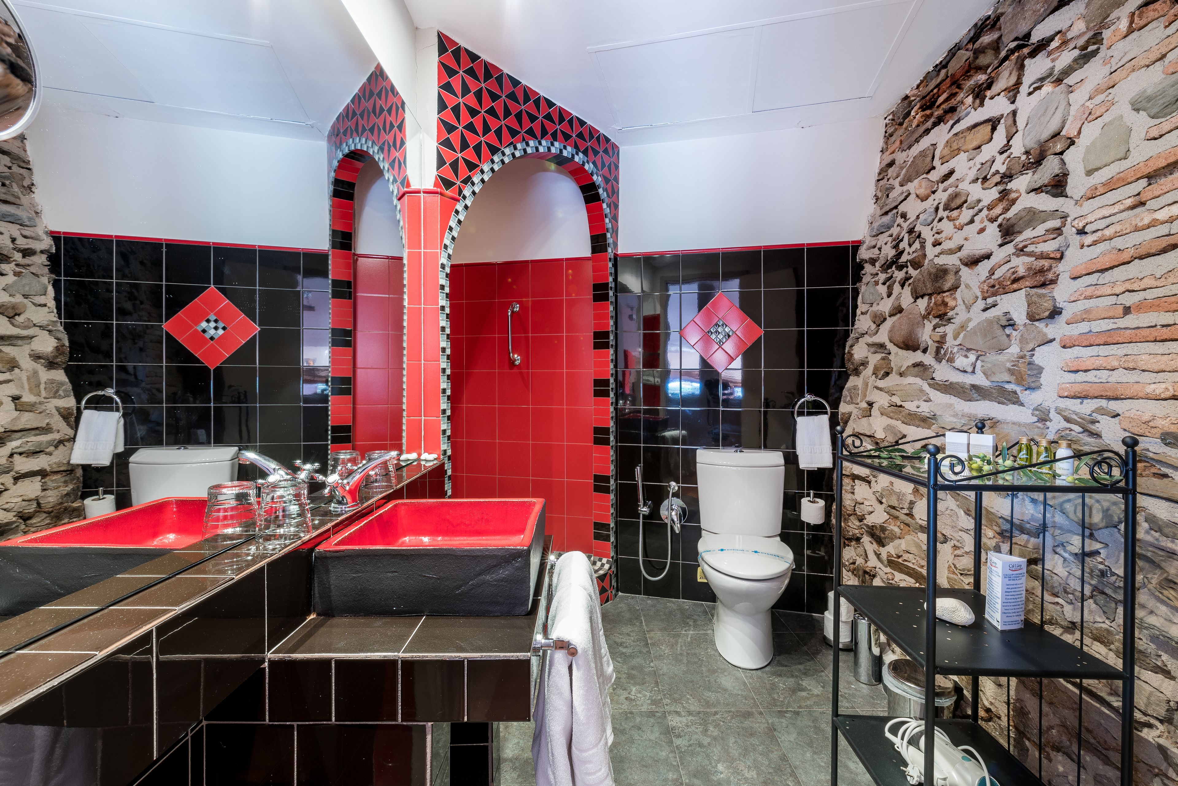 A modern bathroom with a black and red tiled design, a large sink, a toilet, and a shower area.