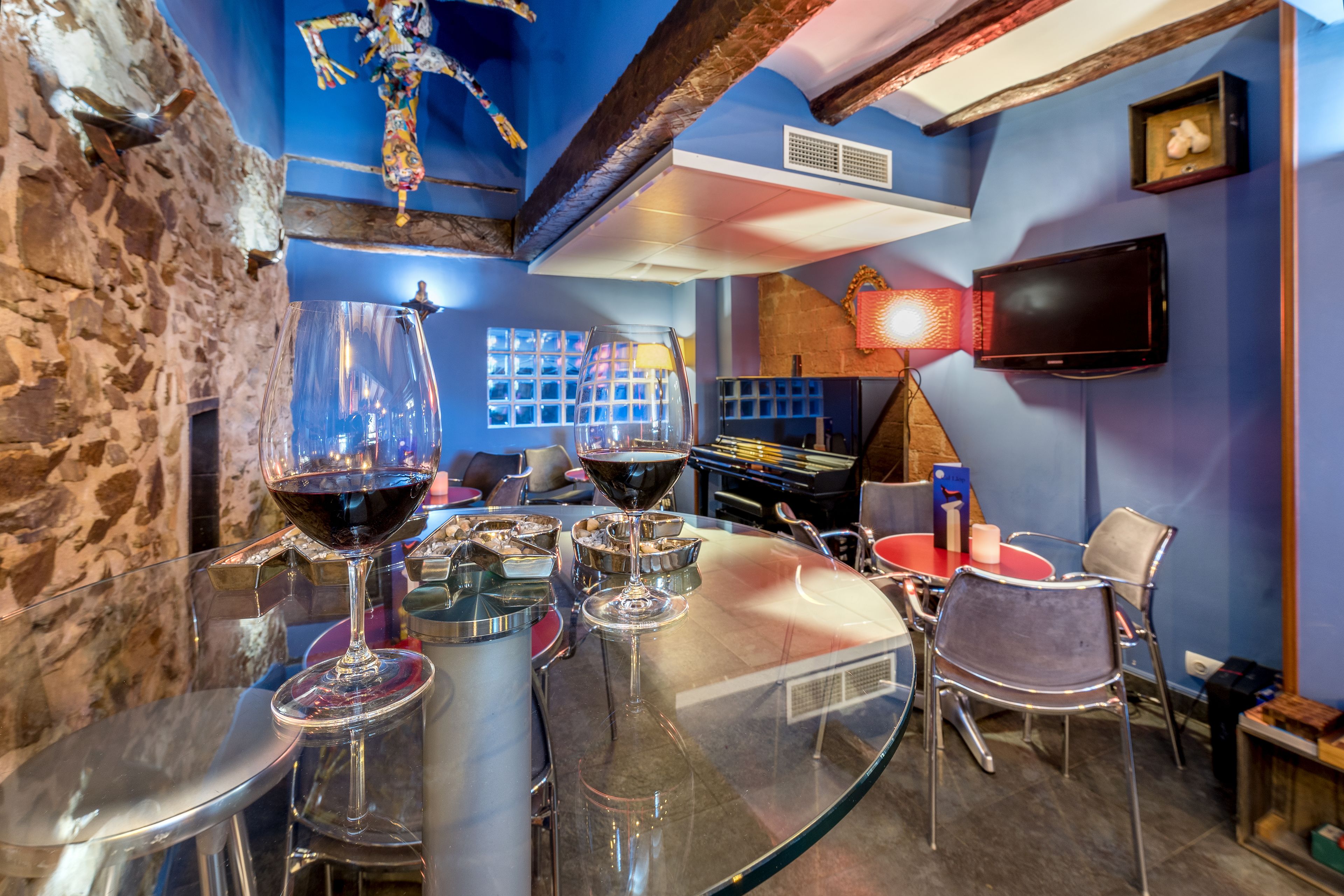 A bar area with a glass table, wine glasses, and a television mounted on the wall.