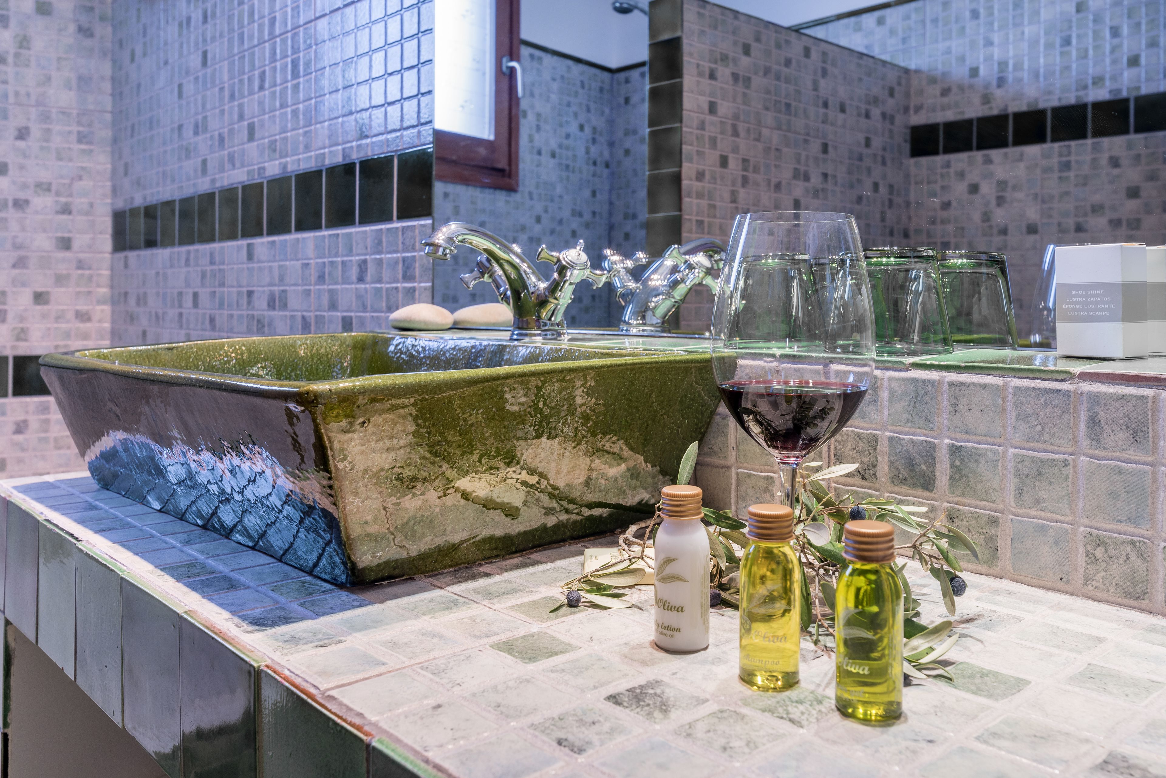 Un baño con un lavabo verde, dos botellas de loción y una copa de vino tinto.