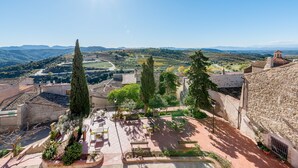Un patio con muros de piedra, una pérgola y vistas del paisaje circundante.