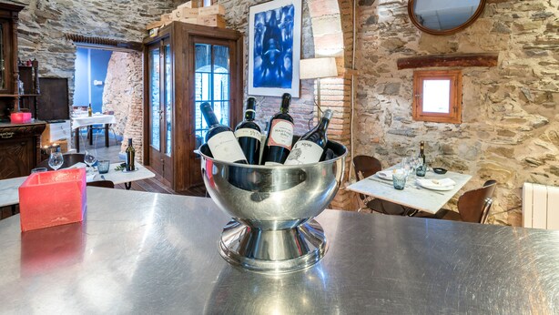 Zona de bar con un bol metálico de botellas de vino, paredes de piedra y una puerta de madera.