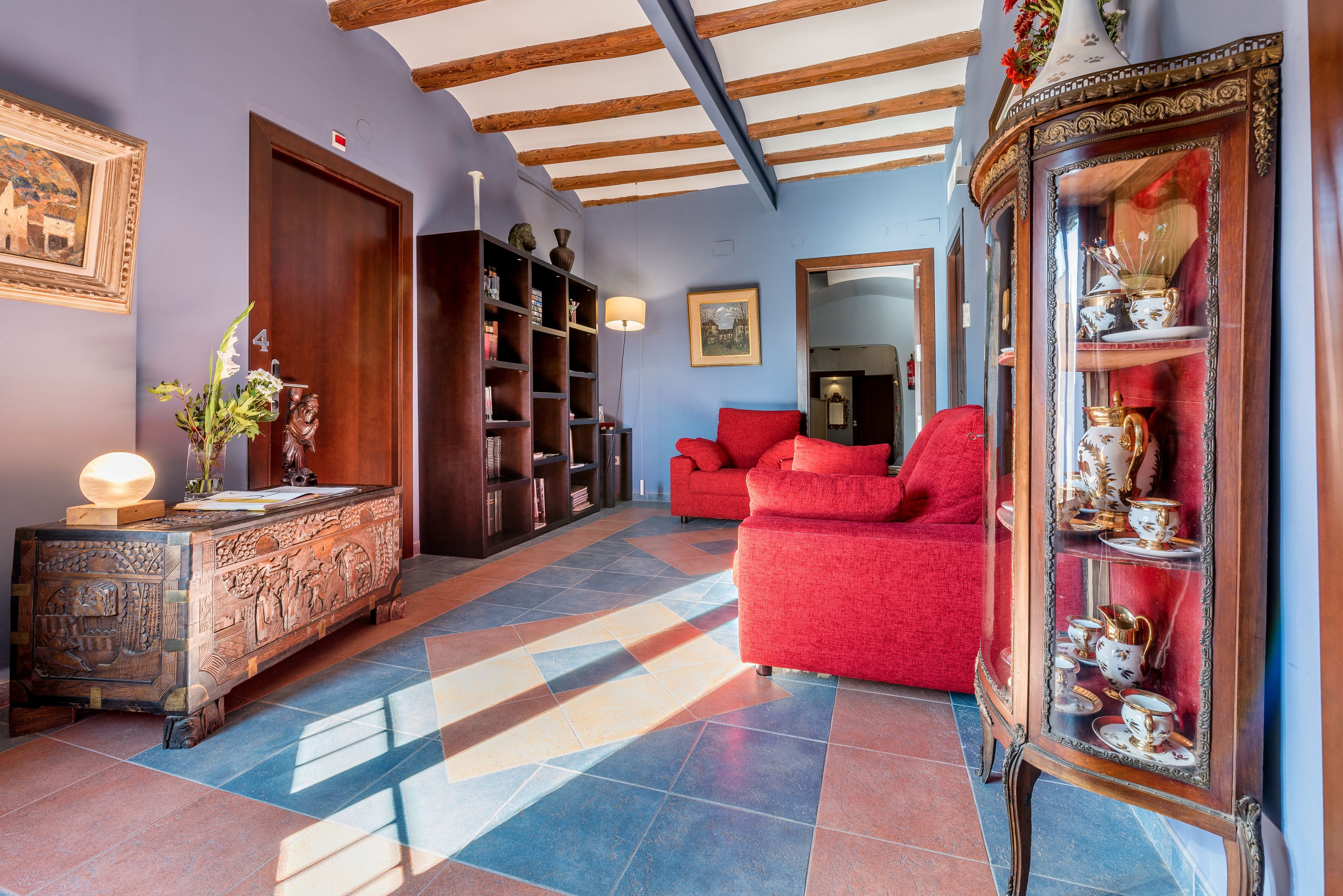 A room with a red sofa, a wooden cabinet with decorative items, and a mirror with a red curtain.
