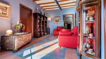 Una habitación con un sofá rojo, un mueble de madera con objetos decorativos y un espejo con cortina roja.
