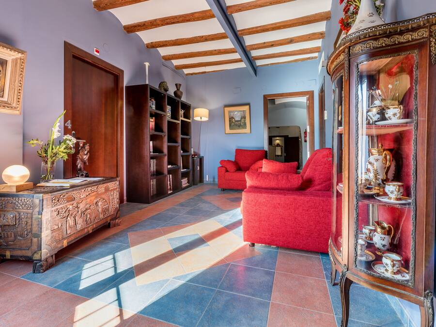 Una habitación con un sofá rojo, un mueble de madera con objetos decorativos y un espejo con cortina roja.