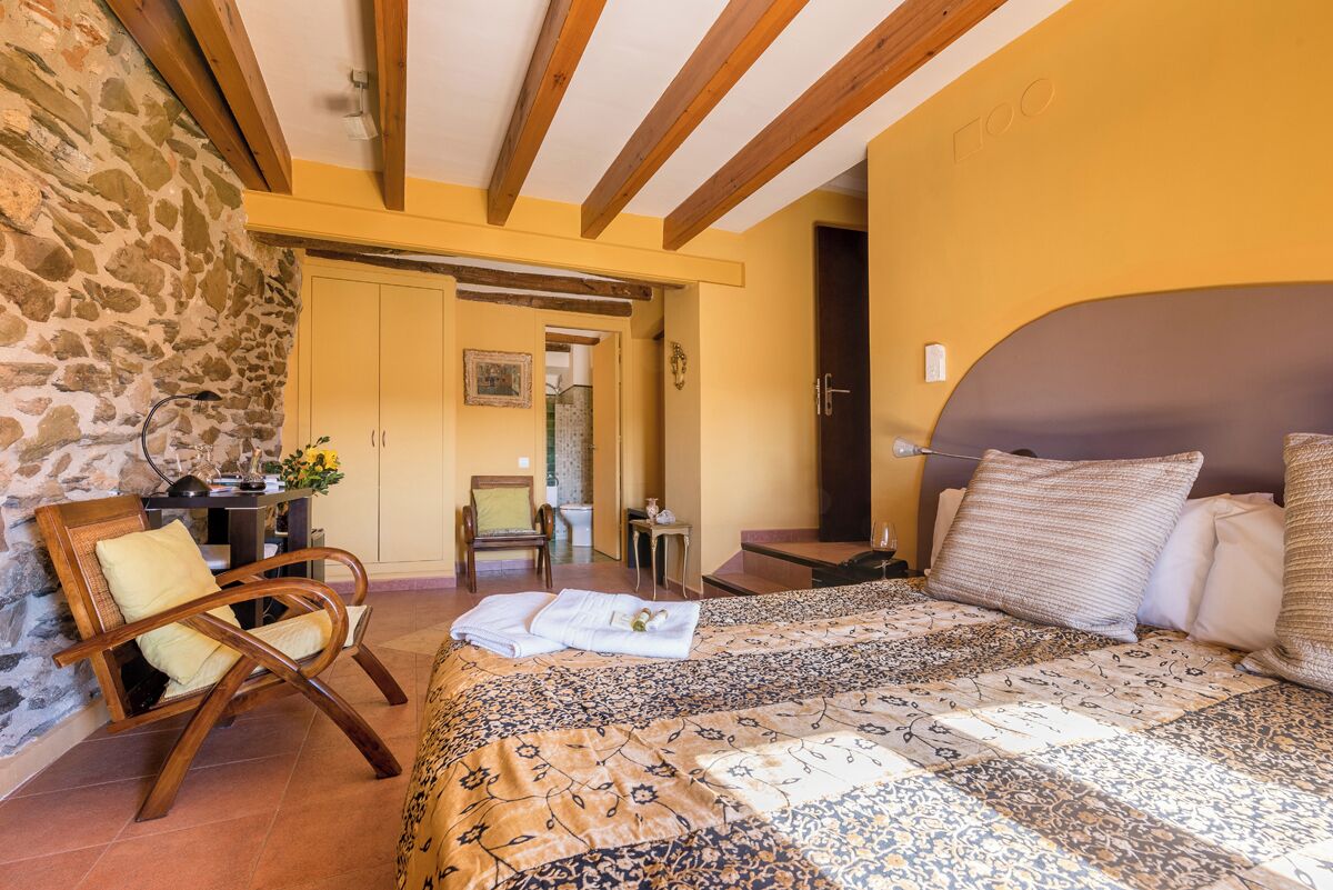 A bedroom with a bed, a chair, a desk, and a stone wall.