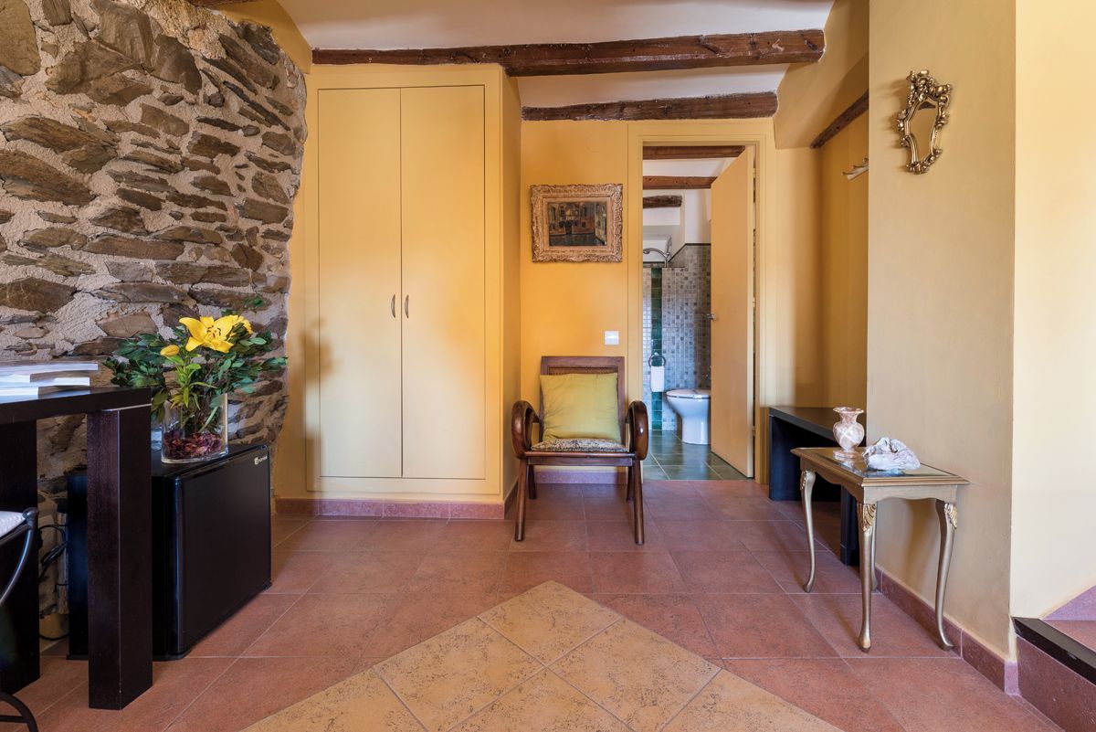 Un pasillo con pared de piedra, una silla de madera, una mesita y un armario.