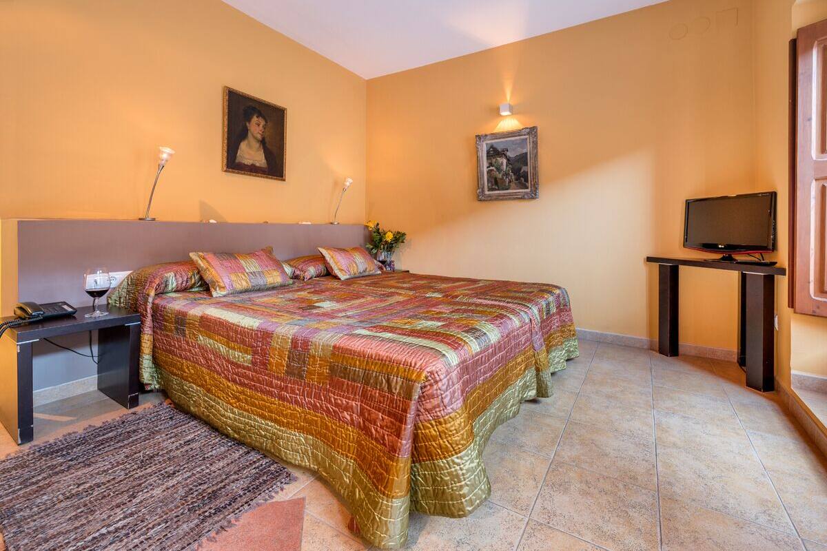 A bedroom with a large bed, a bedside table with a lamp, a TV, and two framed pictures on the wall.