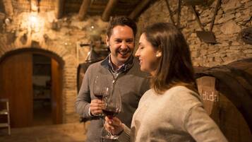 A couple holding wine glasses in a stone-walled room with a wooden door and a hanging light fixture.
