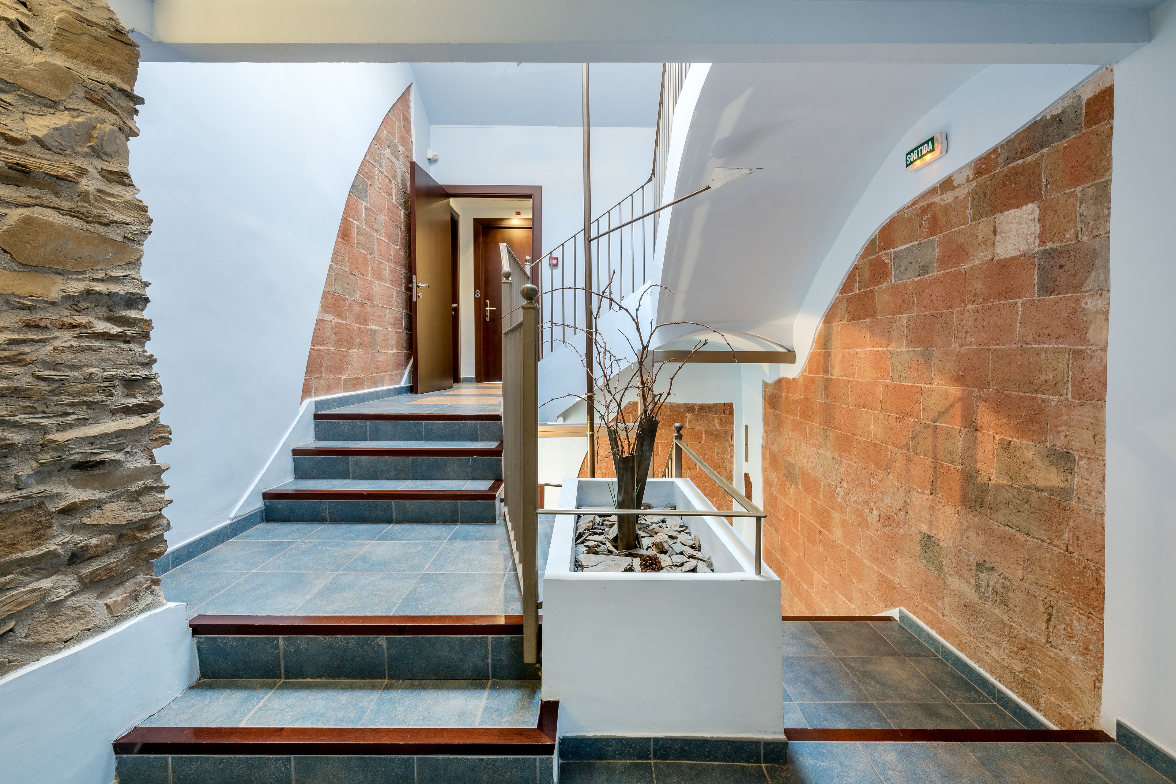 A modern staircase with stone and brick walls, leading to a landing with a door.