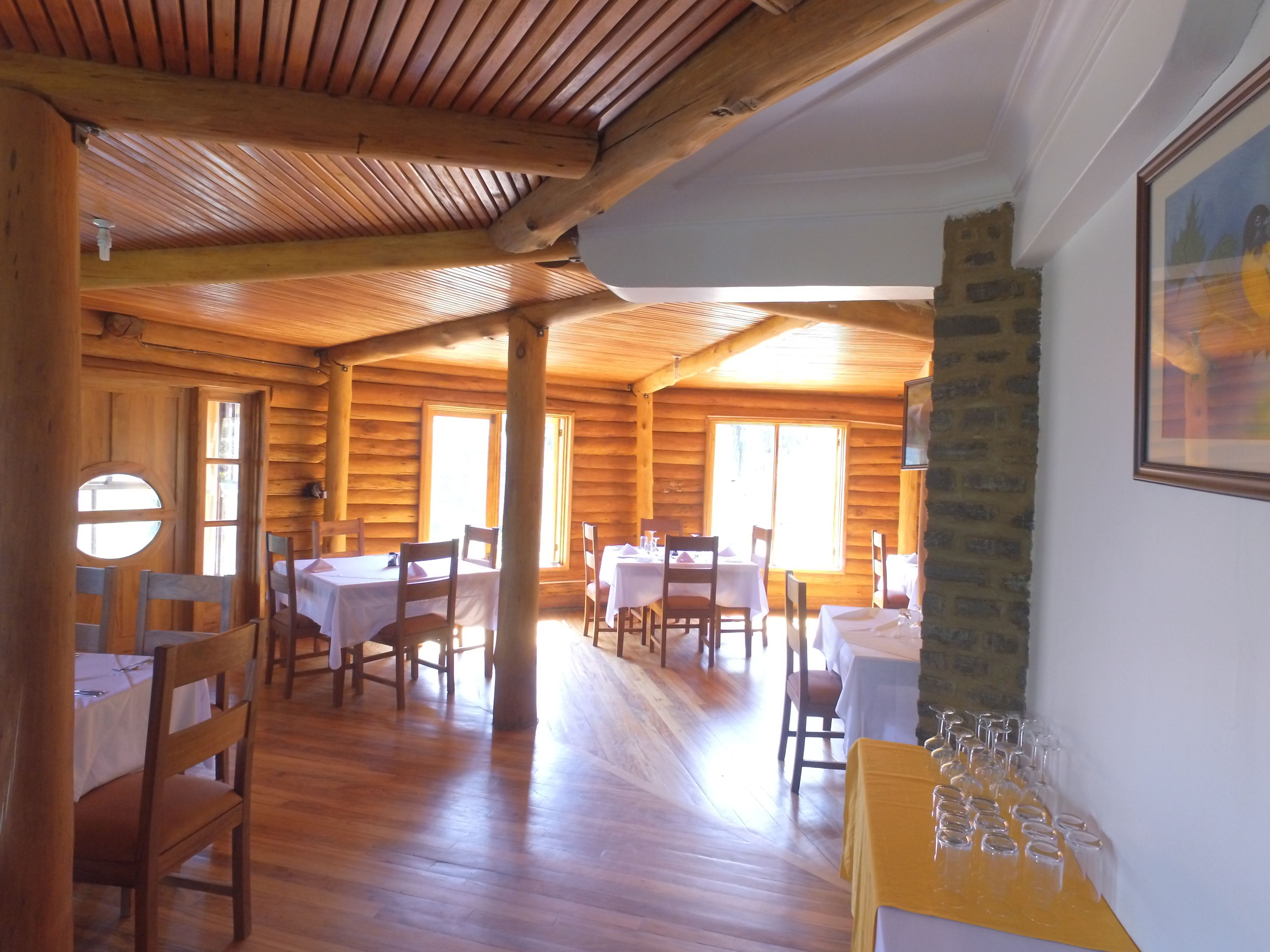 A wooden cabin with multiple dining tables and chairs, a stone pillar, and a painting on the wall.