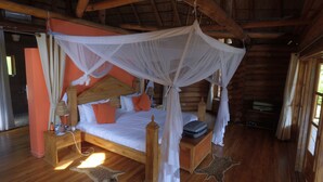 A wooden cabin bedroom with a four-poster bed, a mosquito net, and a wooden headboard.
