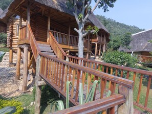 A wooden cabin with a staircase leading to a balcony, surrounded by lush greenery and a thatched roof. - Trackers Safari Lodge Bwindi (Bwindi)