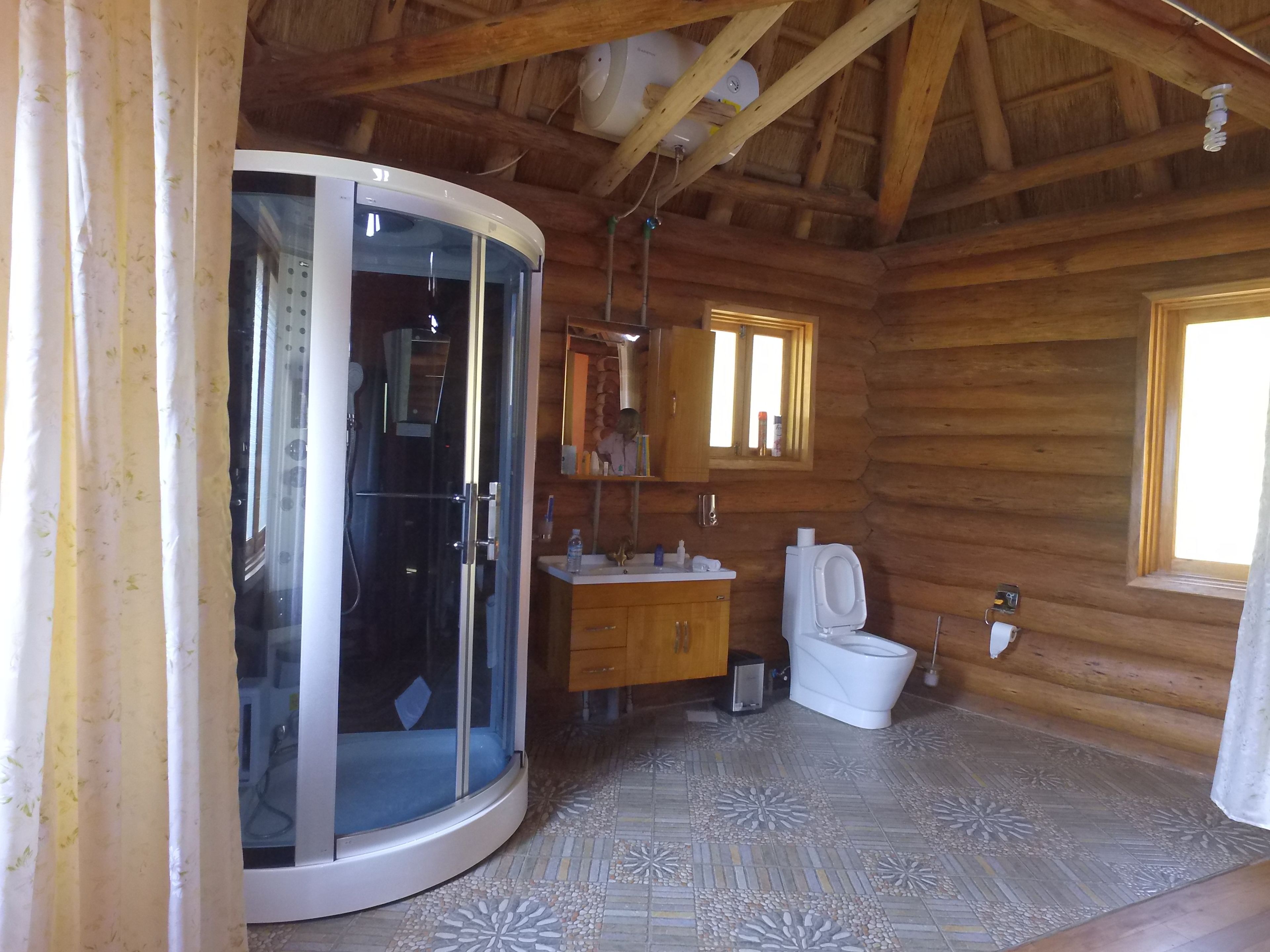 Ein Badezimmer in einer Holzhütte mit einer Duschkabine aus Glas, einem Waschbecken, einer Toilette und einem Fenster.
