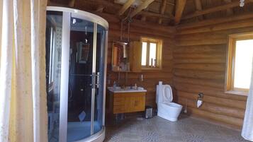 Ein Badezimmer in einer Holzhütte mit einer Duschkabine aus Glas, einem Waschbecken, einer Toilette und einem Fenster.