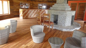 A log cabin interior with a stone fireplace, wicker furniture, and a wooden bar area.