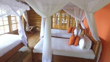 Ein Zimmer mit zwei Betten, jeweils mit weißer Bettwäsche und orangefarbenen Kissen, unter einem Baldachin.