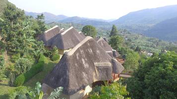 Thatched-roof huts with a wooden deck, surrounded by lush greenery and mountains in the background.