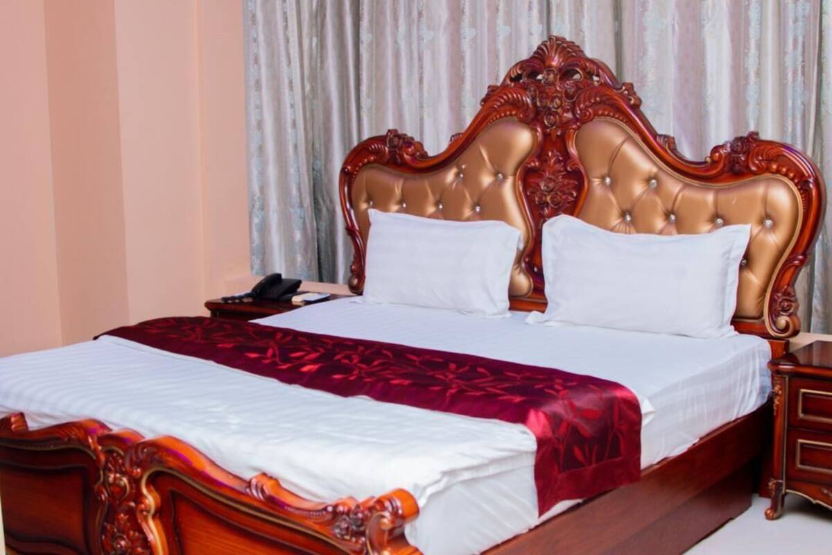 Una cama grande con cabecera capitonada, una manta roja y una mesita de noche de madera con un teléfono.