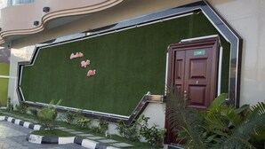 A building facade with a green artificial grass lawn, a red door labeled "CLUB", and a modern architectural design with a curved roof. - Rungwe Hotel (Dar es Salaam)