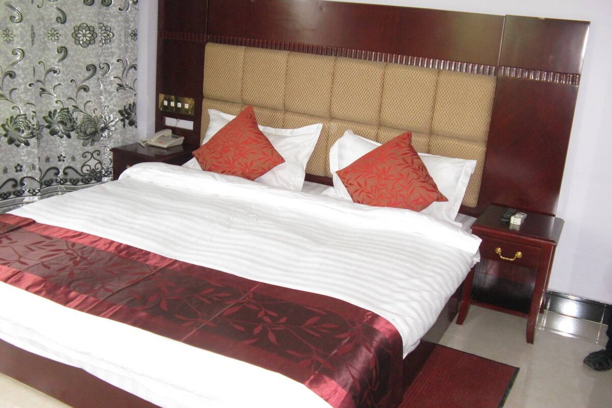Habitación de hotel con una cama grande, dos mesitas de noche y una alfombra roja.